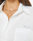 Woman wearing a white shirt with a visible brand logo on a plain background