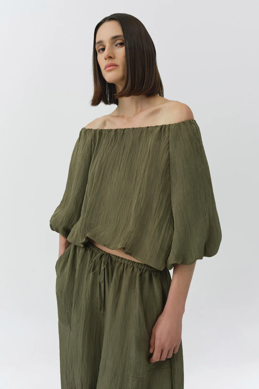 Woman wearing an off-shoulder green top and high-waisted pants on a white background
