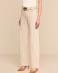 A model wearing a pair of light beige wide-leg jeans with a matching belt featuring a gold buckle, paired with beige pointed-toe heels against a solid beige background.