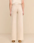 A model shown from the back wearing high-waisted, wide-leg trousers in a light cream or beige color, paired with a textured belt and pointed-toe heels against a solid beige studio background.