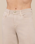 Close-up of a model's lower torso wearing light beige denim jeans against a solid beige background.