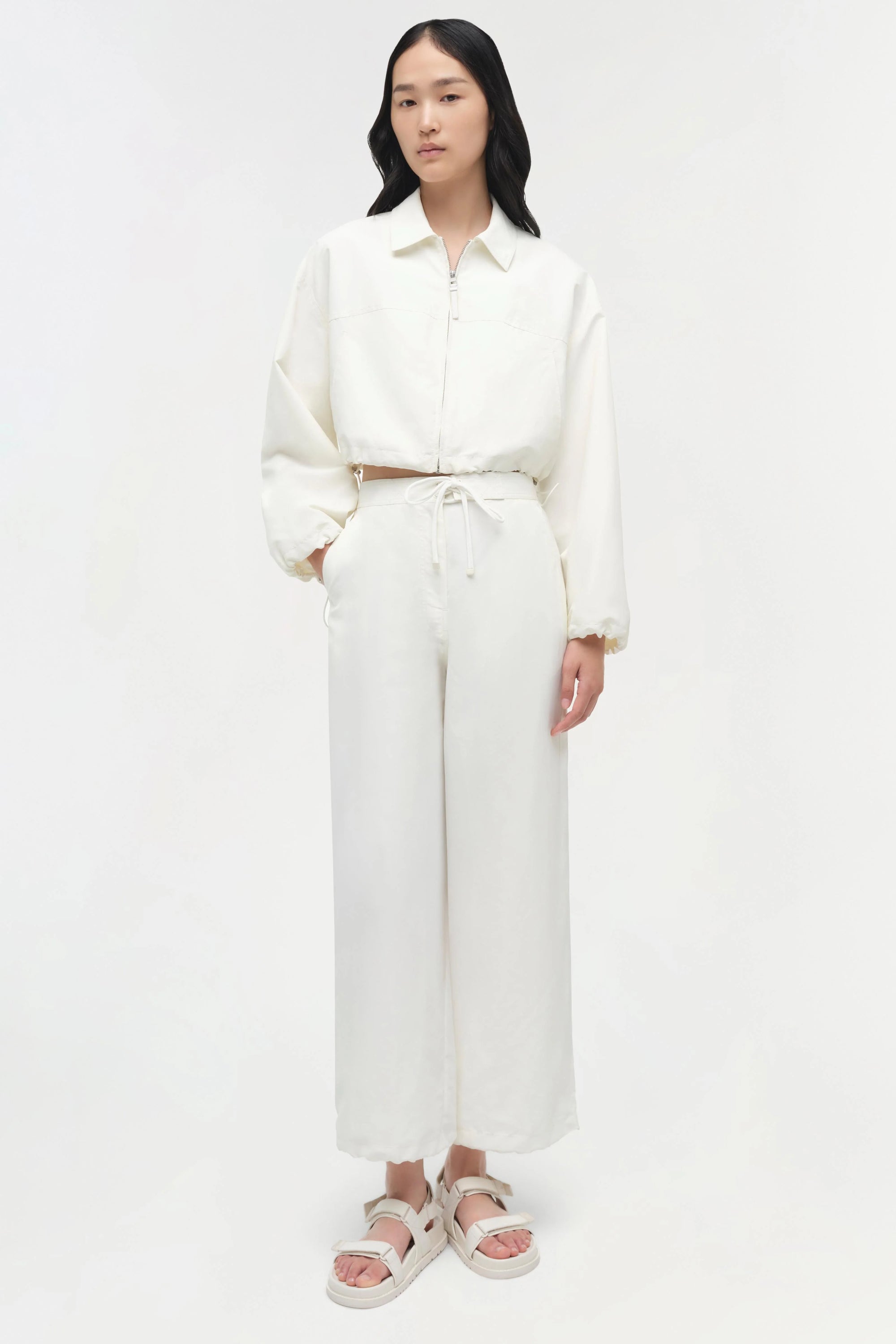 Person wearing a white outfit with straight-leg pants on a plain background