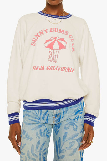 Person wearing a white sweatshirt with 'Sunny Bums Club' text and graphics, paired with blue pants.