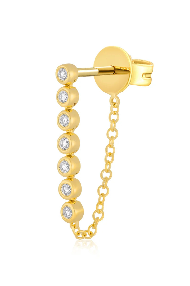 A gold huggie hoop earring featuring a vertical drop chain adorned with seven bezel-set clear round gemstones, shown on a plain white background.