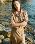 A woman stands on a rocky shoreline with water behind her, wearing Kellen Jacket