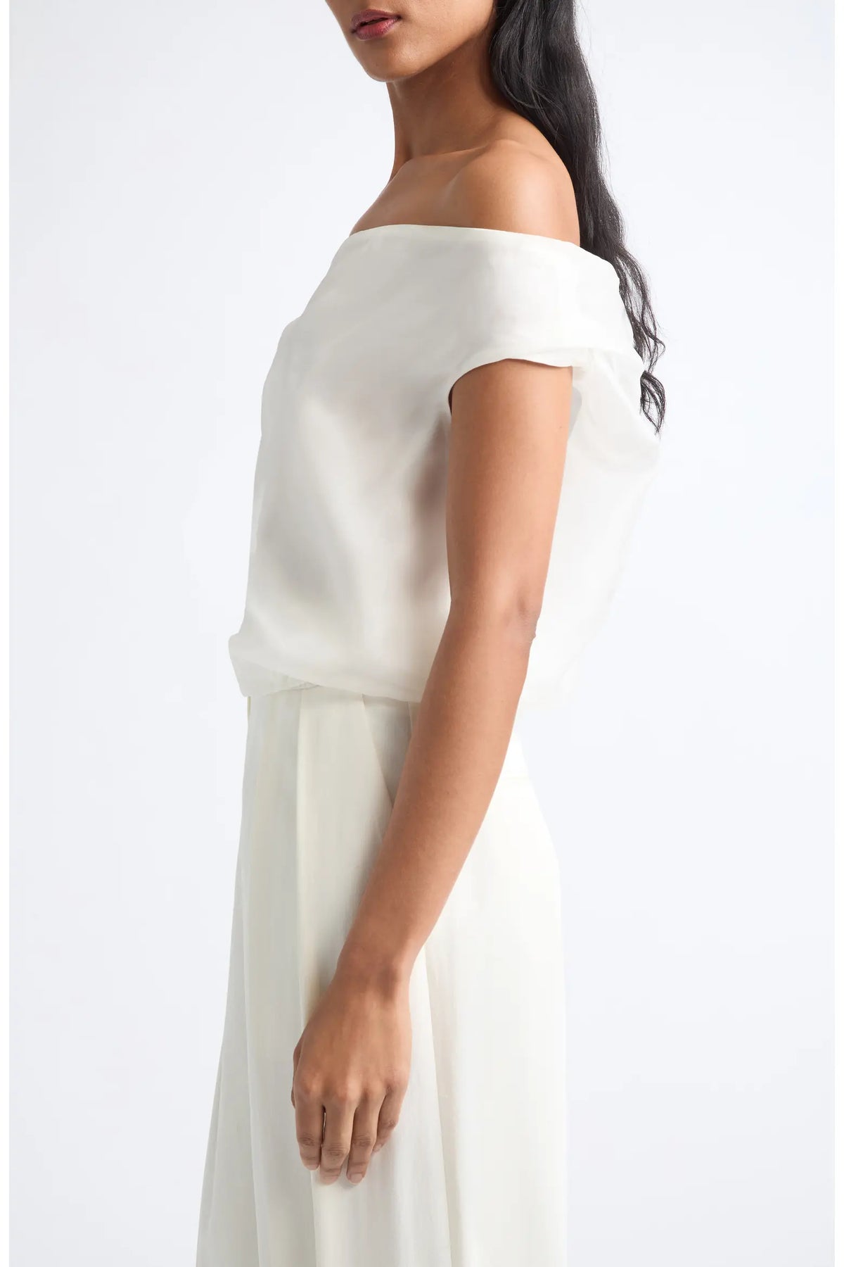 An off-the-shoulder white dress with a draped, layered neckline and a flowing skirt, shown on a model against a plain white background.