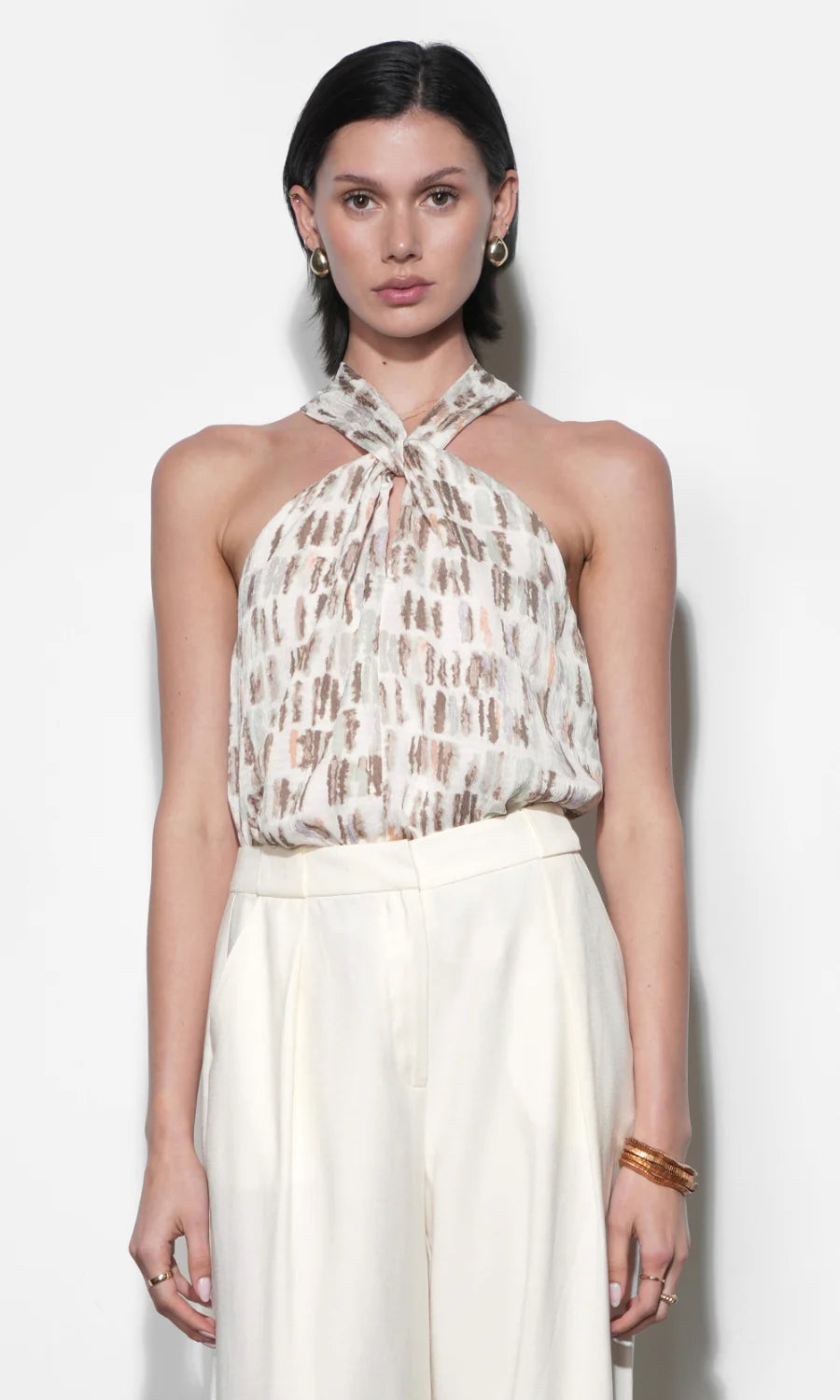 Woman wearing a patterned halter top and white skirt against a plain background