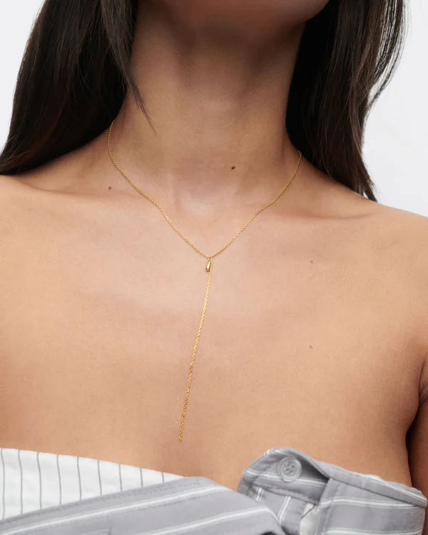 Gold necklace worn by a person on a plain background