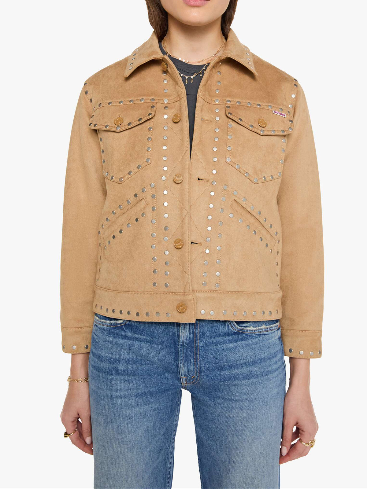 A model wearing a tan suede jacket with silver studded details, paired with blue jeans and sunglasses, against a plain white background.
