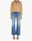 A model wearing a tan suede studded jacket, blue flare jeans, and silver heeled sandals, standing against a plain white studio background.