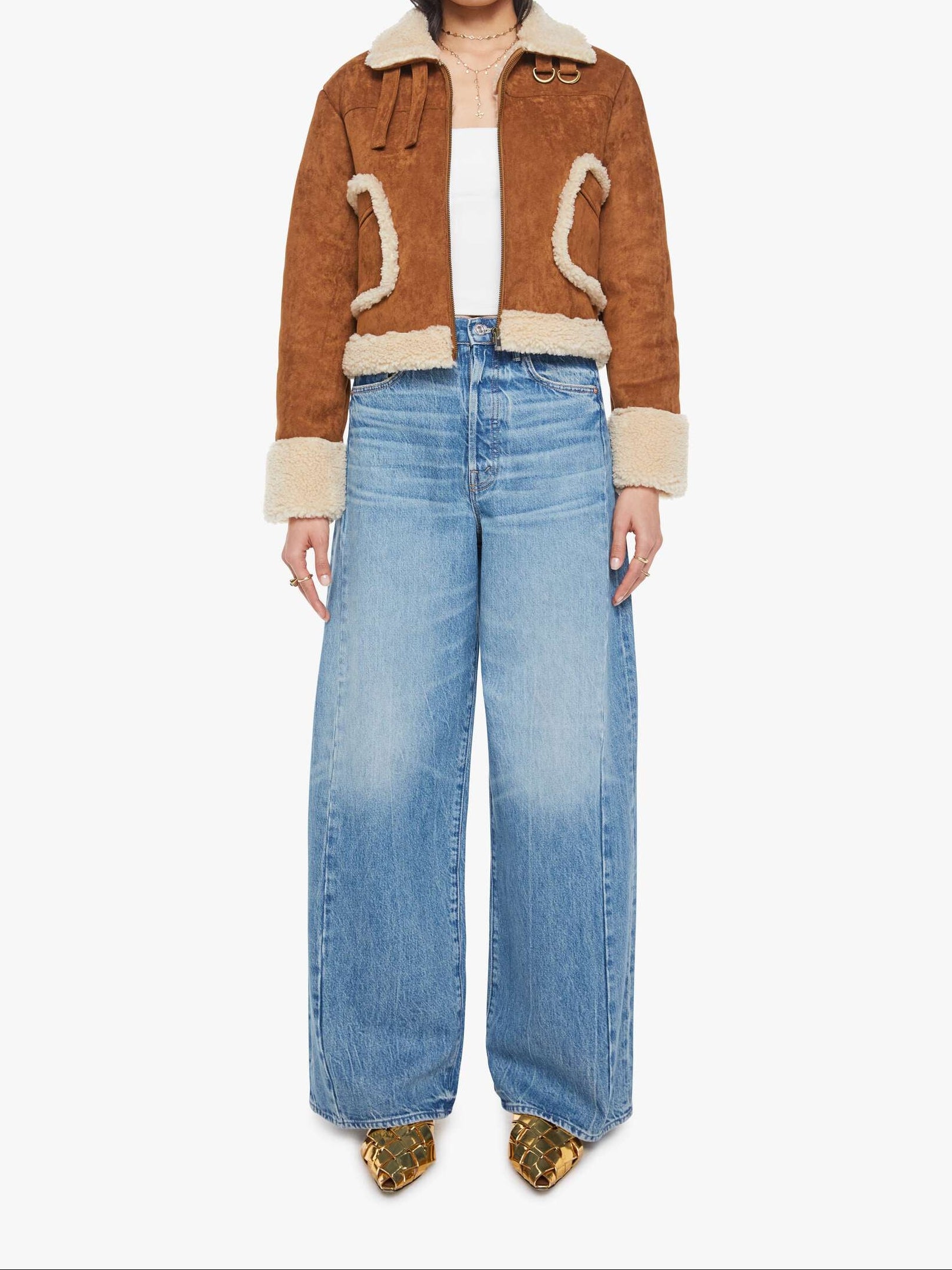 Person wearing a brown jacket with white fur trim and blue jeans on a white background