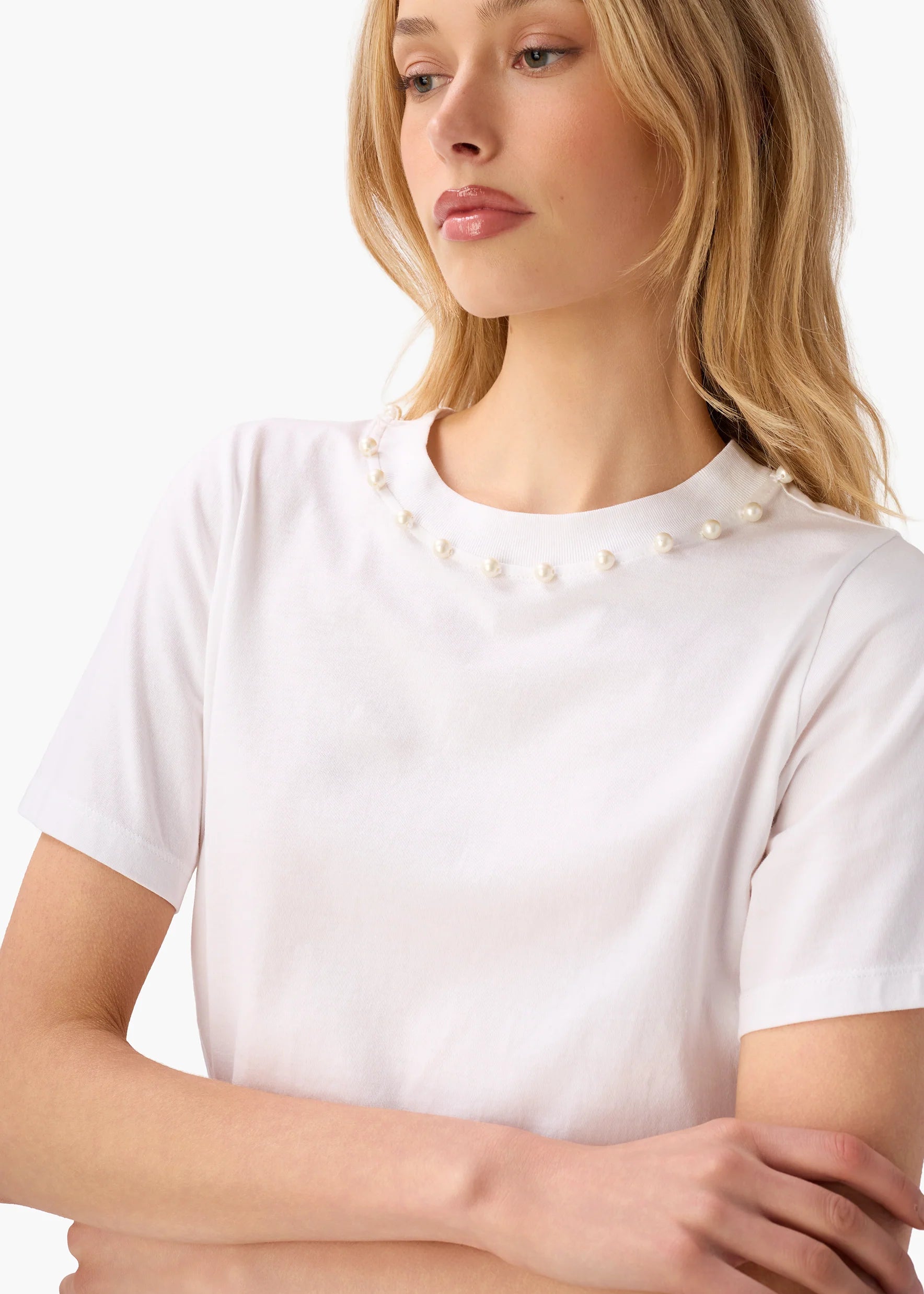 Woman wearing a white t-shirt with pearl embellishments on a plain background