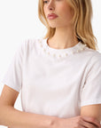 Woman wearing a white t-shirt with pearl embellishments on a plain background