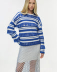 Woman wearing a blue and white striped sweater with fringe details on a white background