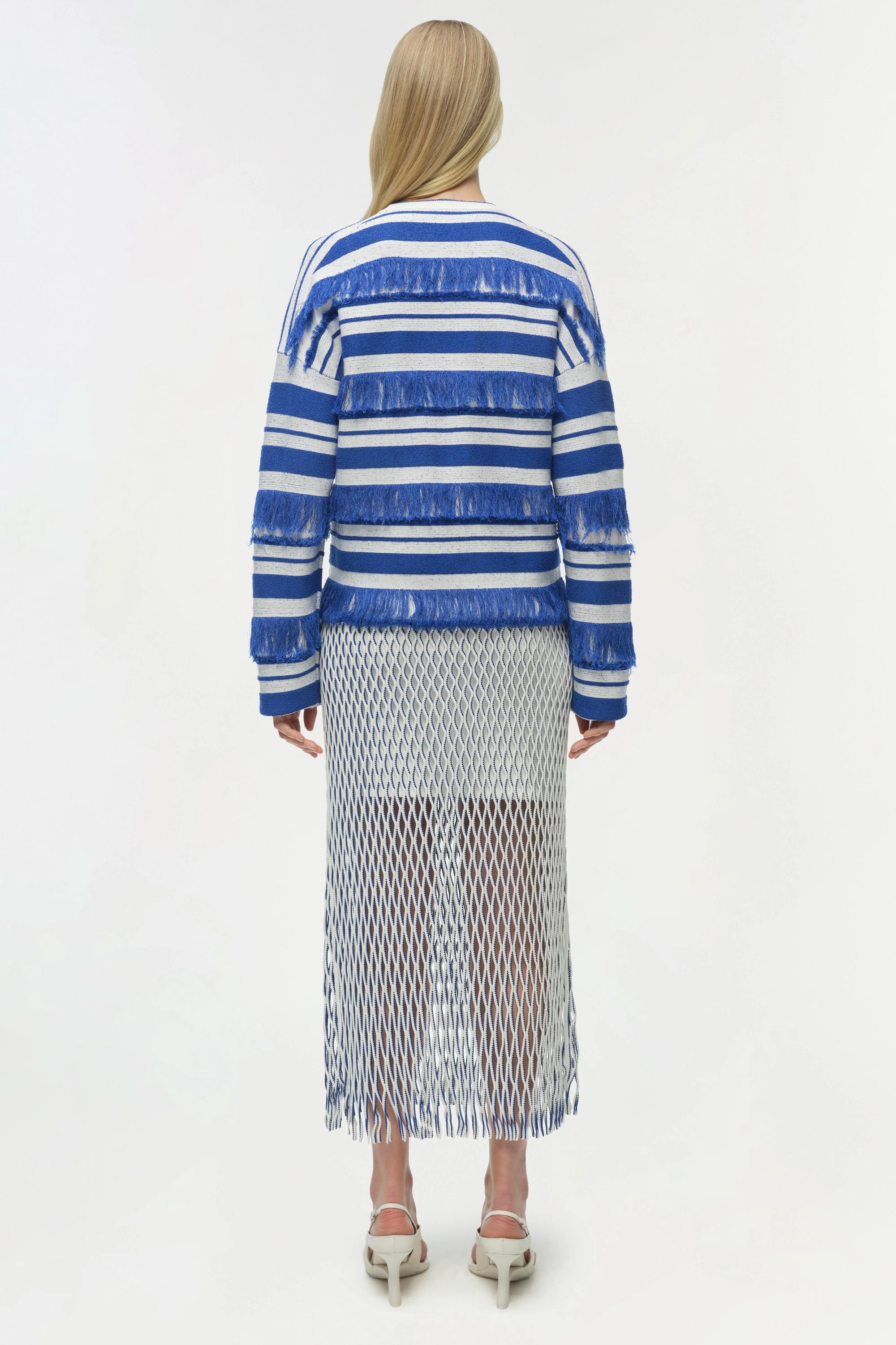 Woman wearing a blue and white striped sweater with a pleated skirt on a white background