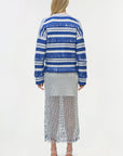 Woman wearing a blue and white striped sweater with a pleated skirt on a white background
