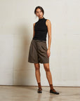 Woman wearing a black sleeveless top and brown shorts against a white wall front view