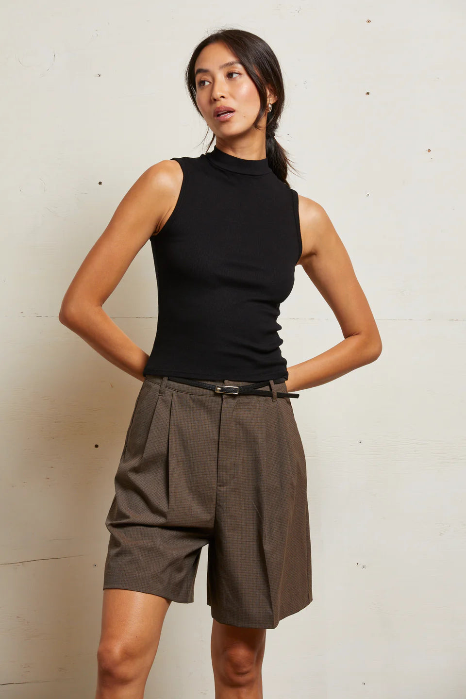 Woman wearing a black sleeveless top and brown shorts against a light background front view