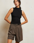 Woman wearing a black sleeveless top and brown shorts against a light background front view