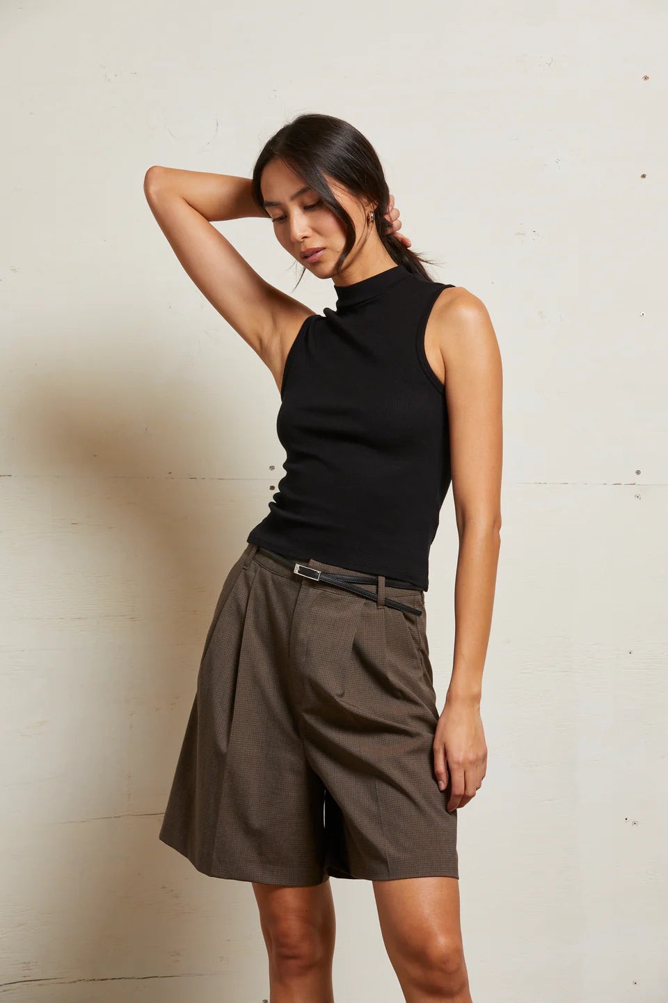 Woman wearing a black sleeveless top and brown pleated skirt against a plain background front view