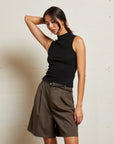 Woman wearing a black sleeveless top and brown pleated skirt against a plain background front view