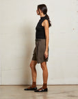 Woman wearing a black sleeveless top and brown shorts against a white wall side view