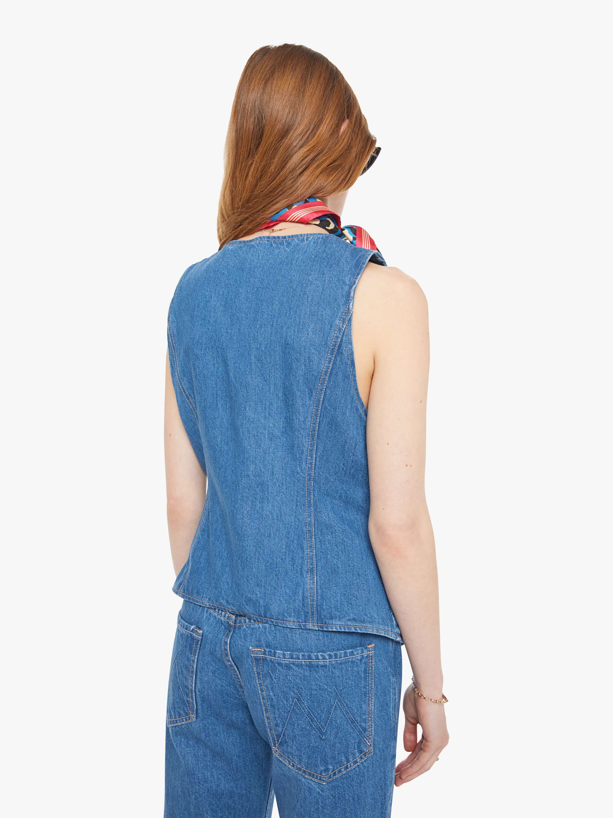 Woman wearing a blue denim vest and pants with a red and blue patterned scarf around her neck on a white background. back view