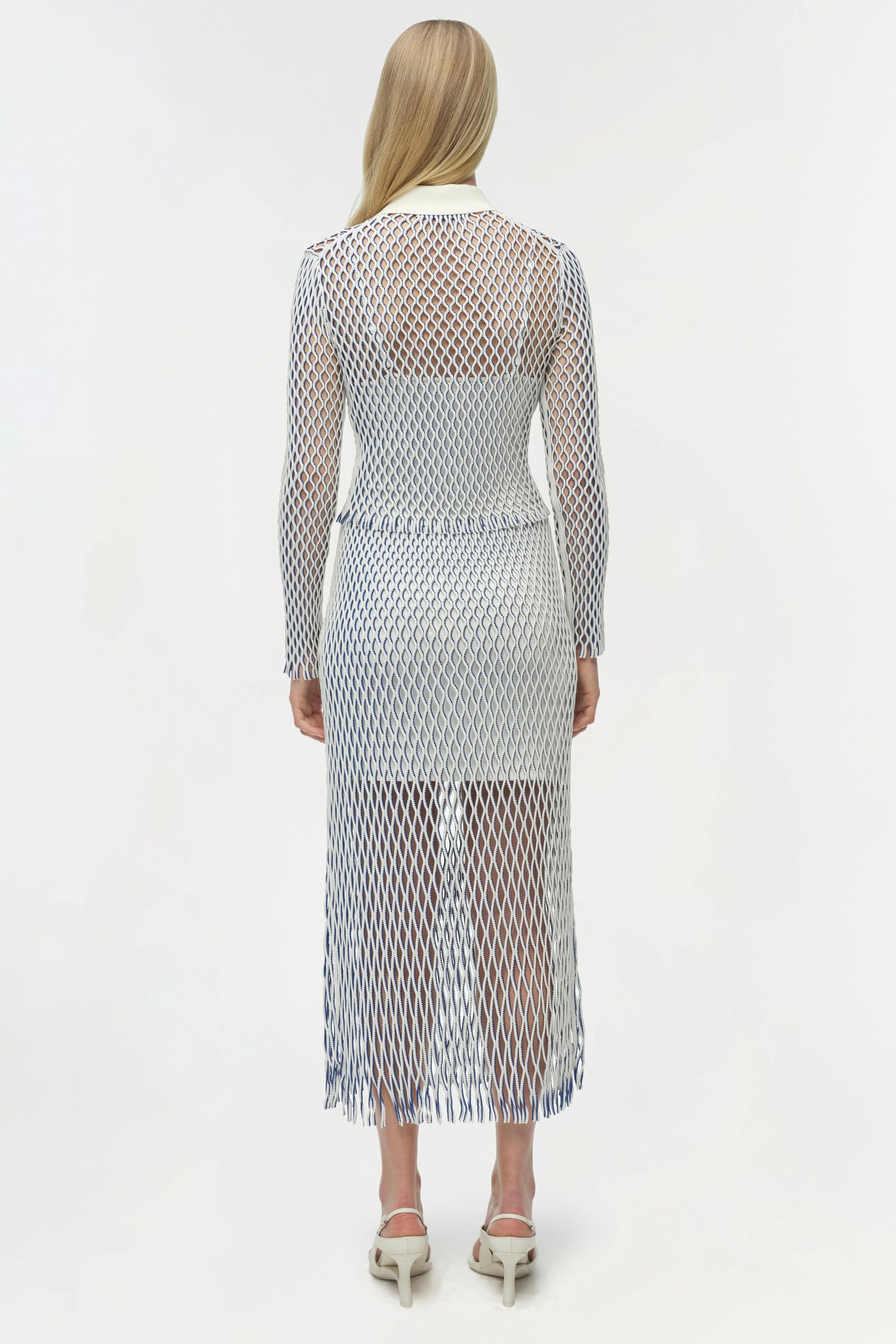 Woman wearing a long, sheer fishnet dress with a white background