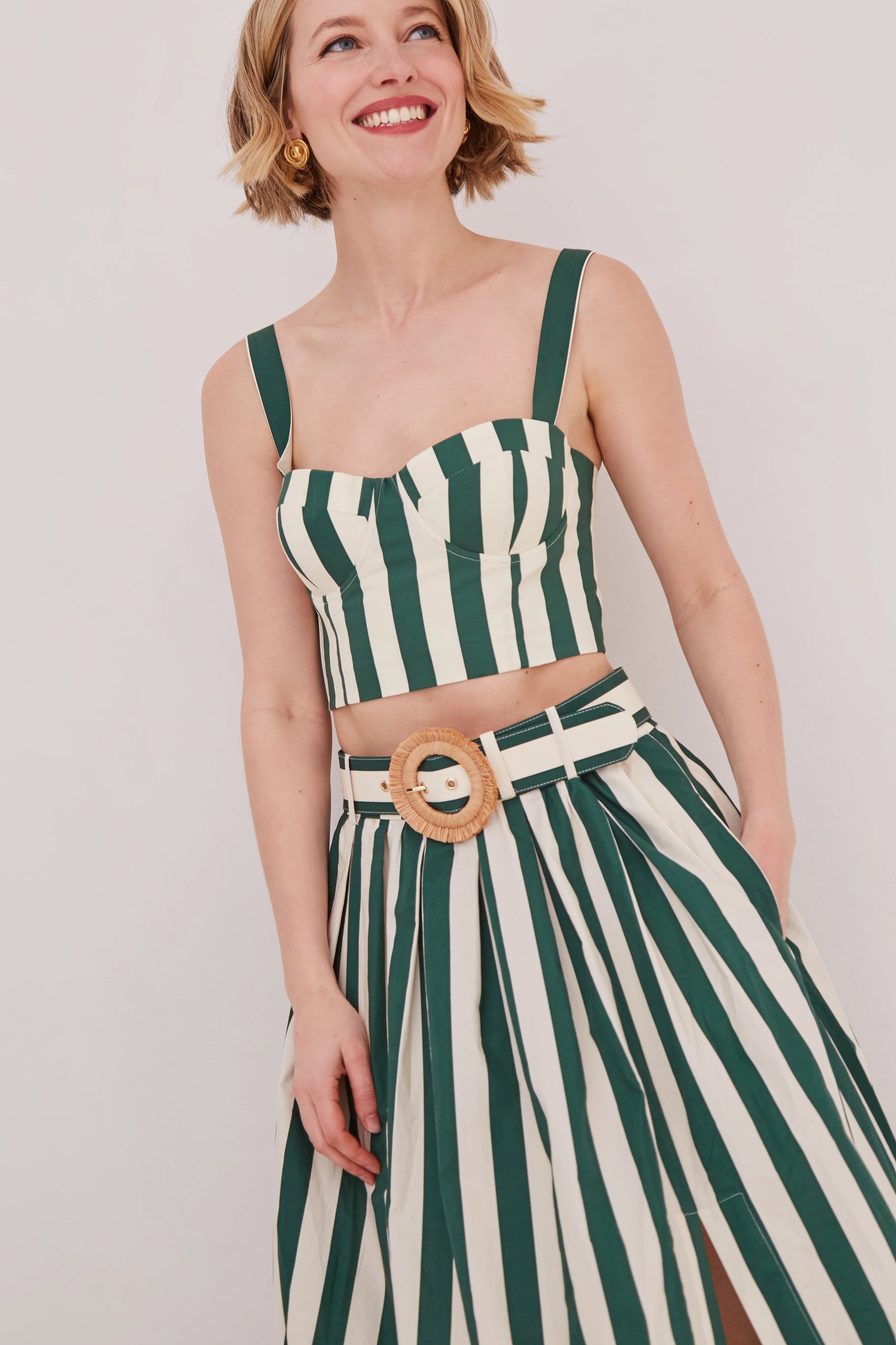 Woman wearing a green and white striped matching set with a belt on a plain background