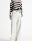 A model wearing a gray and black horizontally striped long-sleeve knit sweater paired with high-waisted, wide-leg white trousers, shot against a plain white studio background.