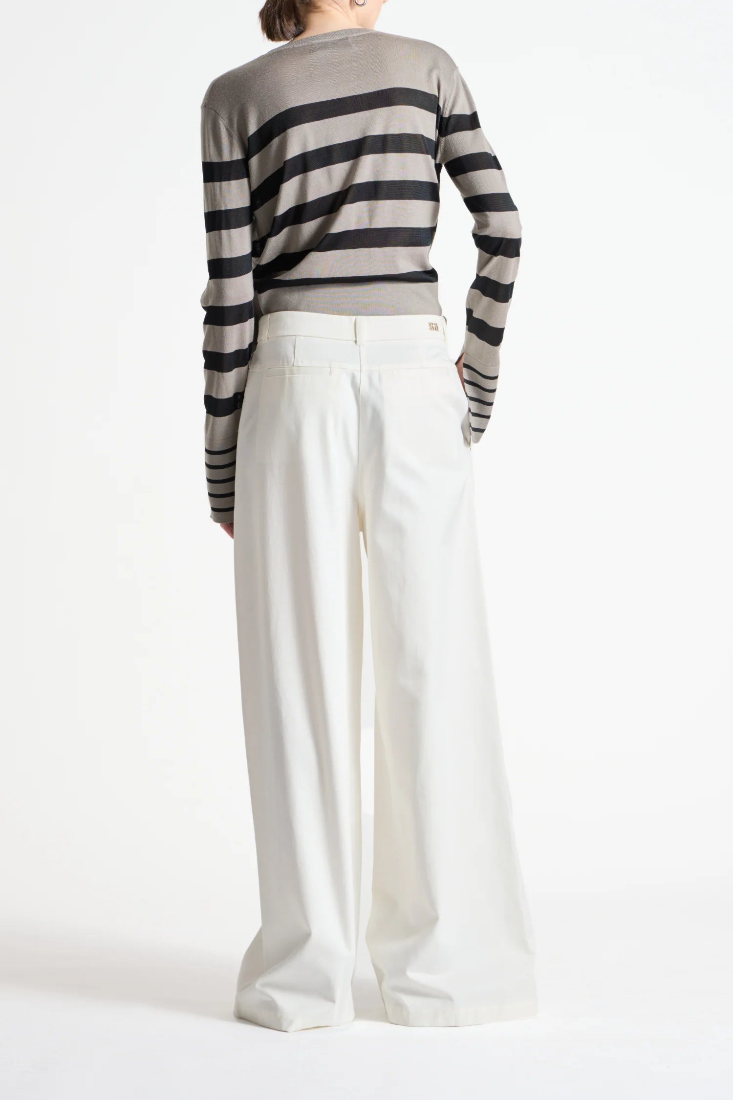Person wearing a striped sweater and white pants on a white background