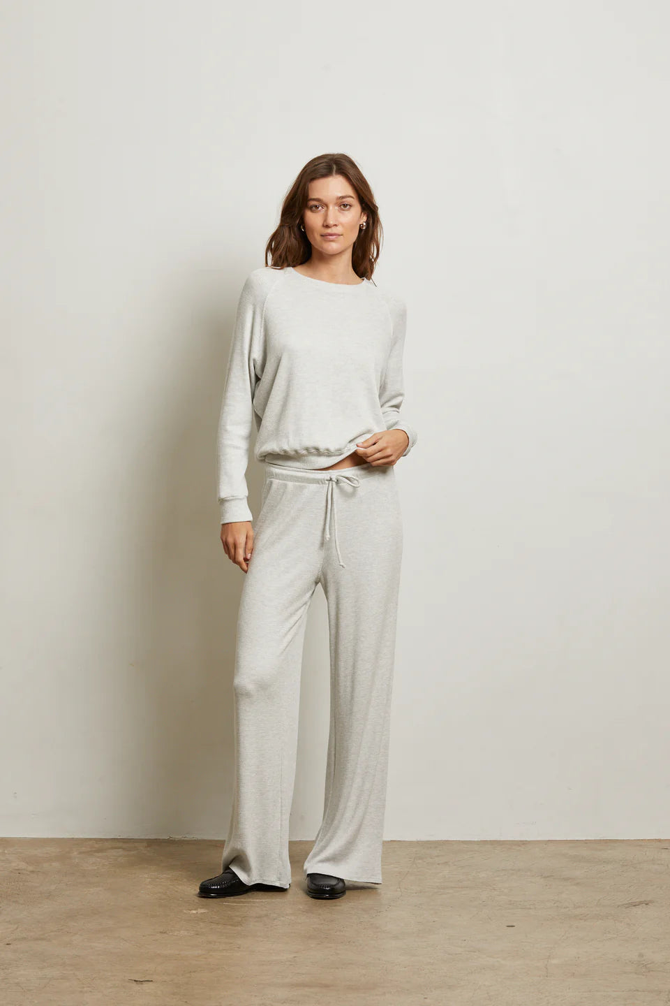 Woman wearing a light gray sweater and pants against a white background front view