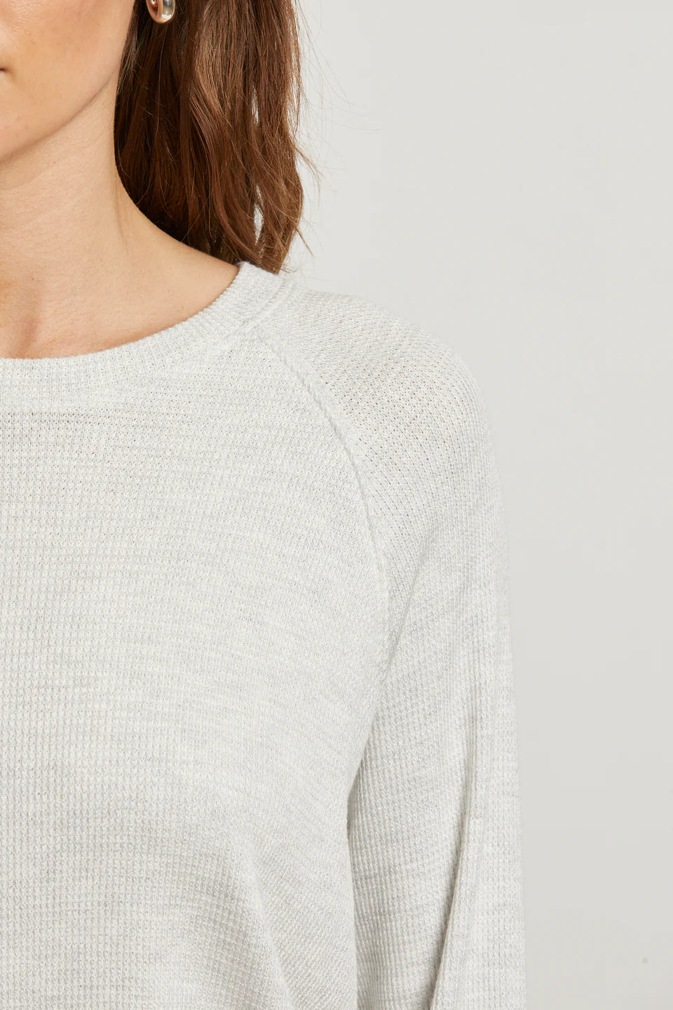 Close-up of a person wearing a light gray sweater on a plain background detail view