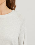 Close-up of a person wearing a light gray sweater on a plain background detail view