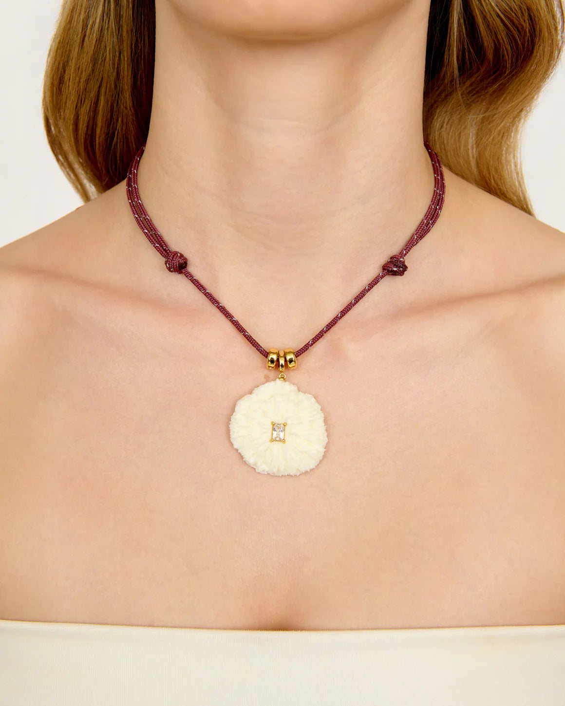 Necklace with a circular shell pendant featuring a square symbol on a plain background