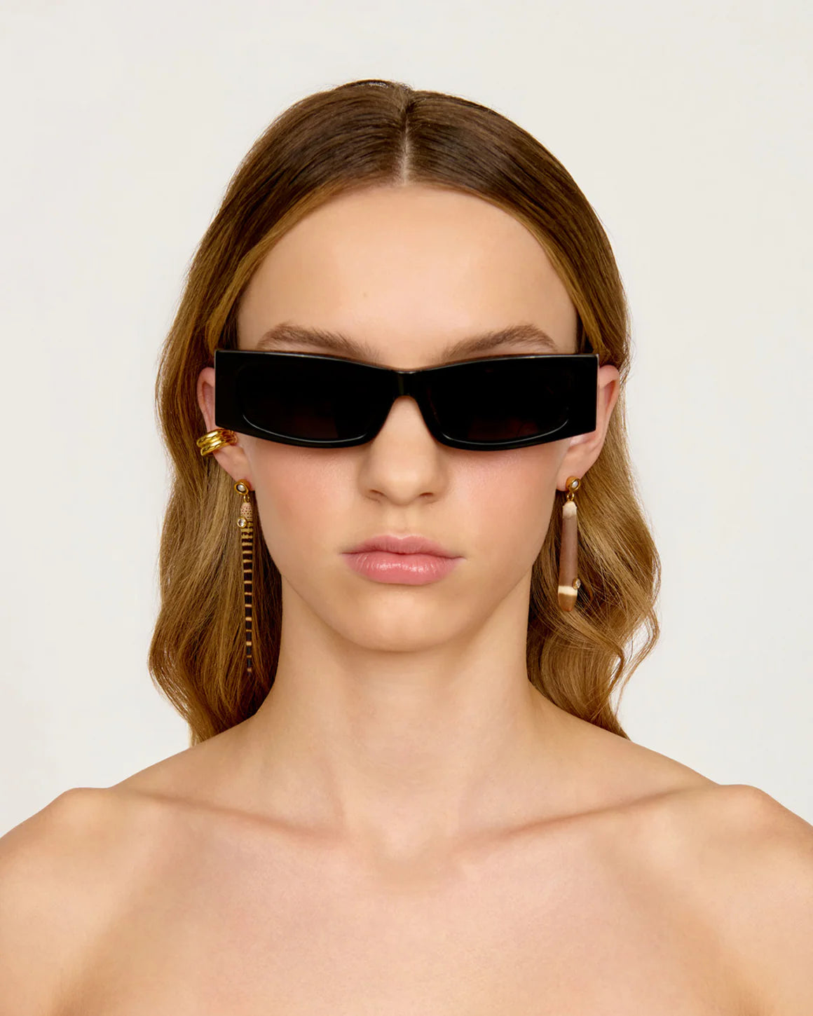 Woman wearing black sunglasses and gold earrings against a white background
