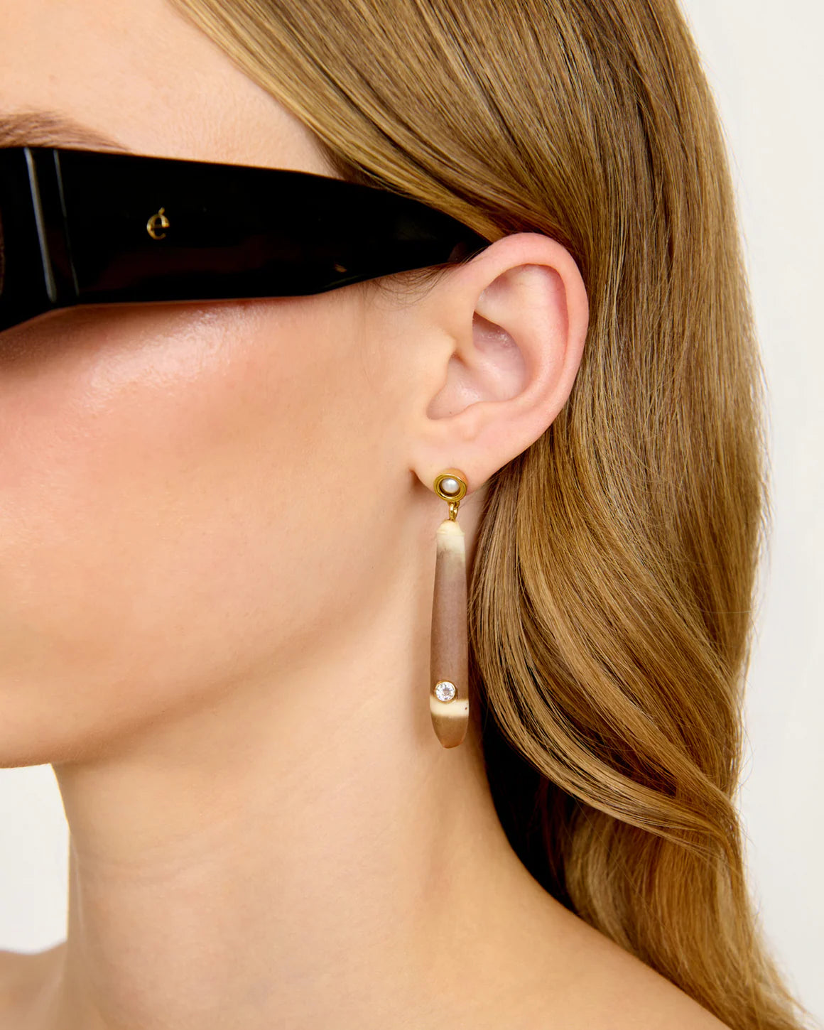 Close-up of a person wearing gold shell earrings with a neutral background