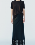 model wearing a black maxi skirt with fringe trim and a short sleeve brown tee on a white background