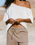 Woman wearing a white off-shoulder top and beige pants in a desert setting