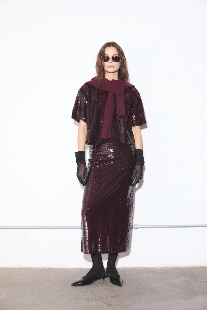 Model wearing a burgundy sequin outfit with sunglasses and gloves against a white background