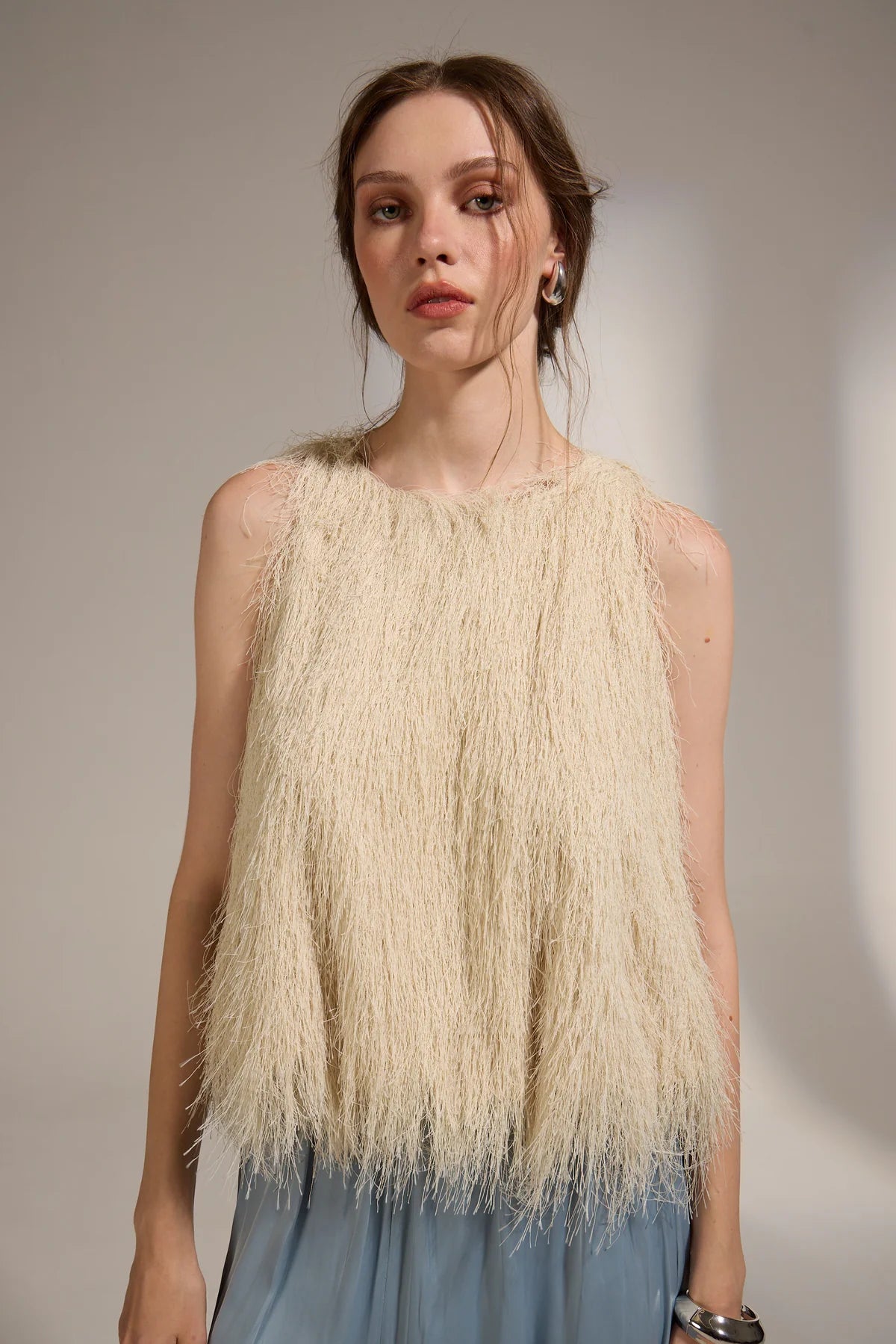 Woman wearing a beige fringed top against a plain background