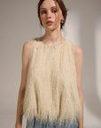 Woman wearing a beige fringed top against a plain background