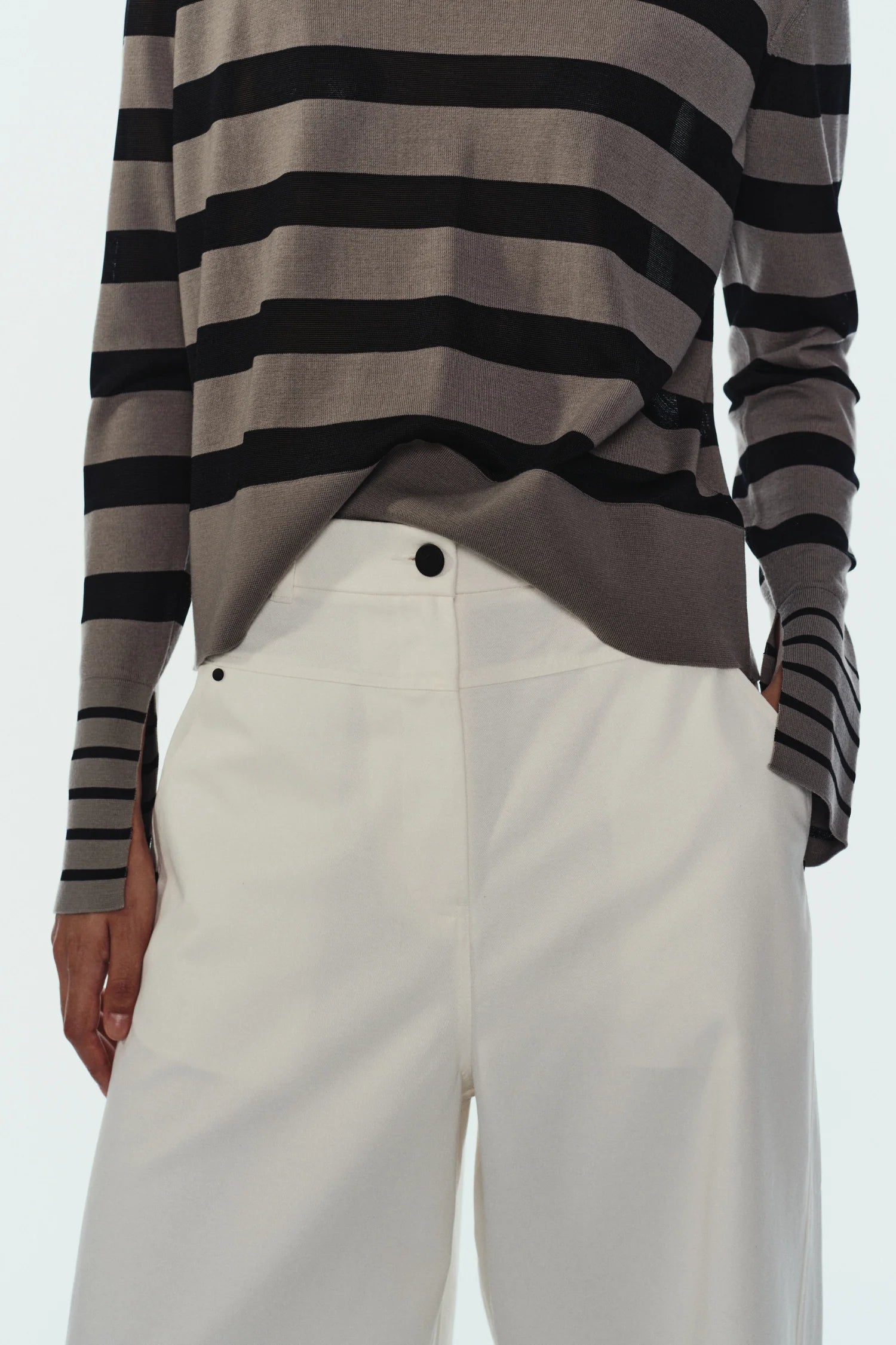 Person wearing a gray and black striped long-sleeve shirt with white pants on a light gray background