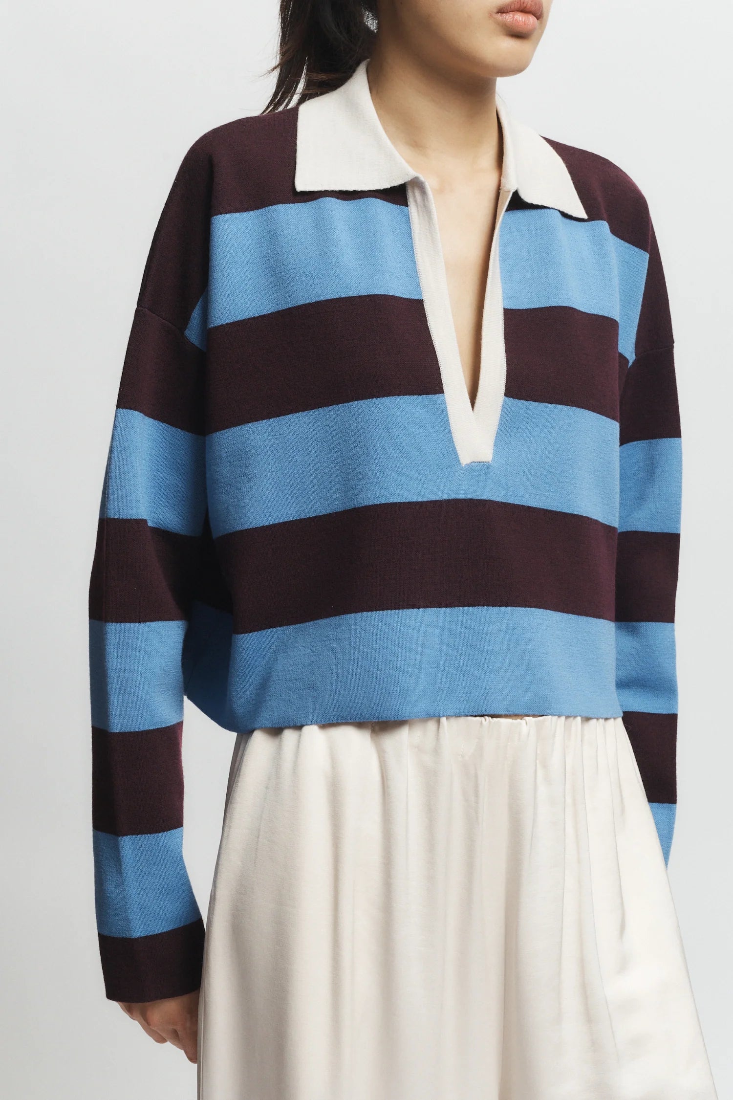 Person wearing a blue and brown striped shirt with a white collar on a plain background