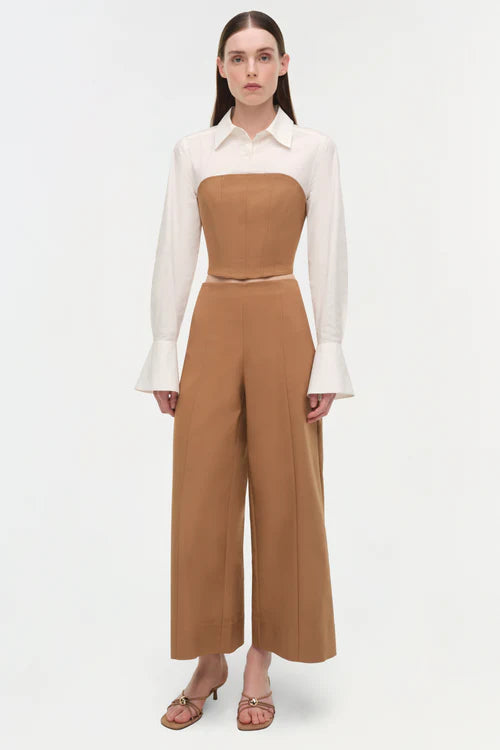 Woman wearing a white blouse and brown high-waisted pants on a white background