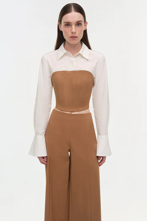Woman wearing a white blouse with a brown top and wide-leg pants on a white background