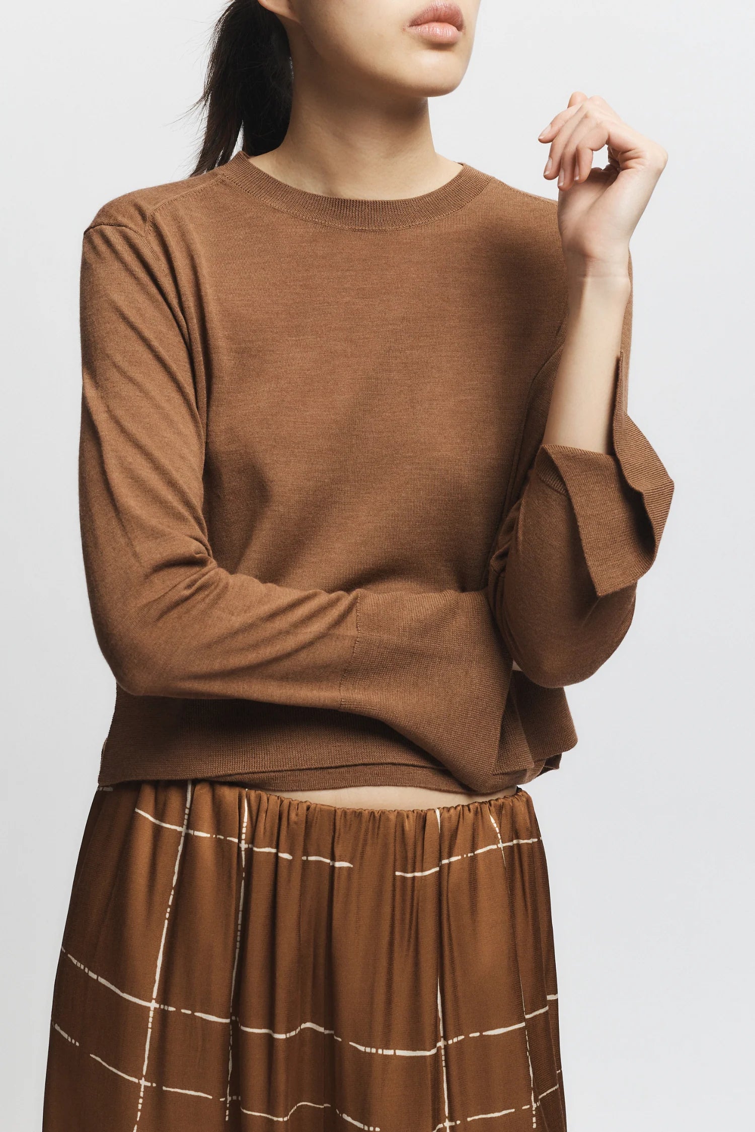 Person wearing a brown sweater and plaid skirt on a white background