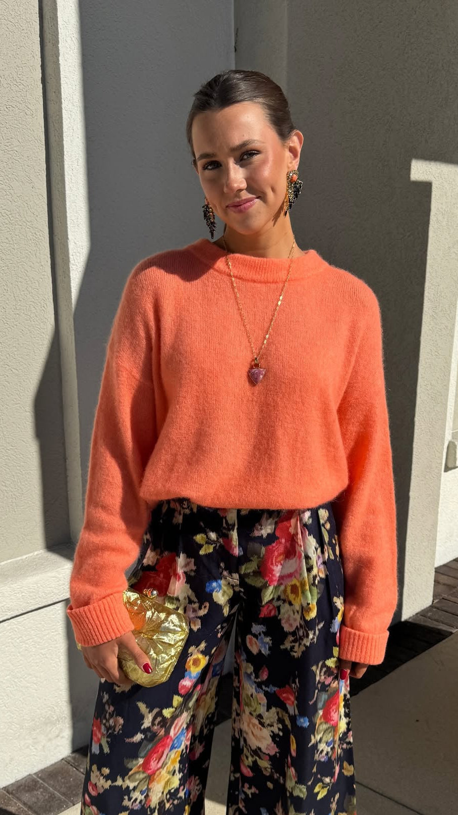 Woman wearing an orange sweater and floral pants standing outdoors.