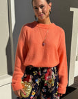 Woman wearing an orange sweater and floral pants standing outdoors.