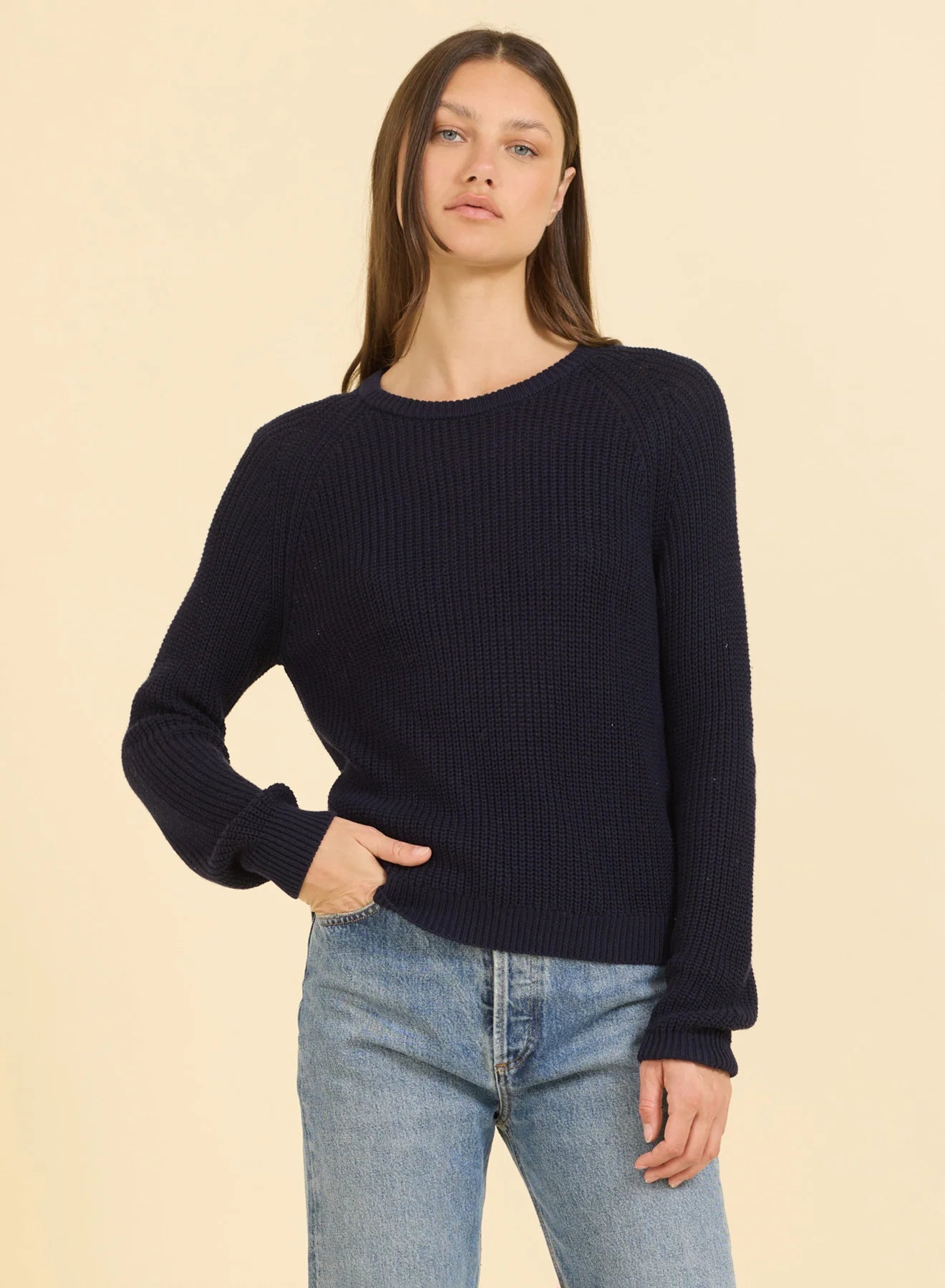 Woman wearing a navy sweater and blue jeans against a beige background